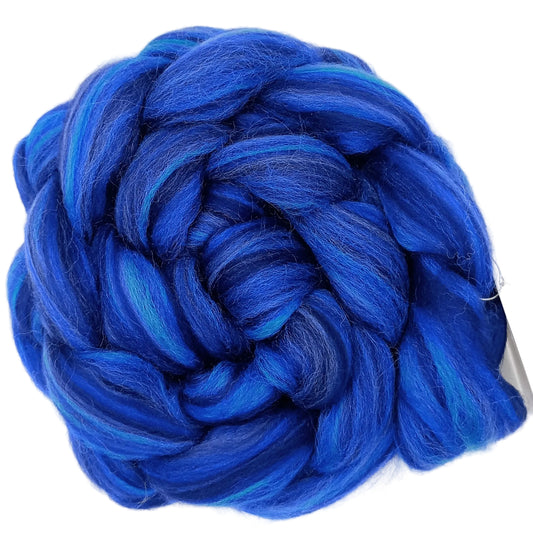 A coiled bundle of vibrant blue and royal blue variegated wool roving, likely for knitting or weaving, photographed on a clean white background.