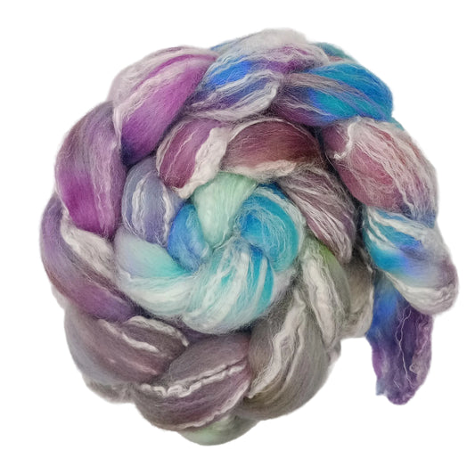 A coiled bundle of soft, twisted fiber roving in a variegated pastel colorway of purple, blue, mint green, white, and gray, photographed on a plain white background.